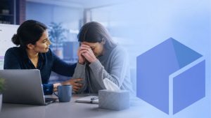 A manager comforting an employee at her desk during a compassionate leave conversation, with a laptop and tissues on the table